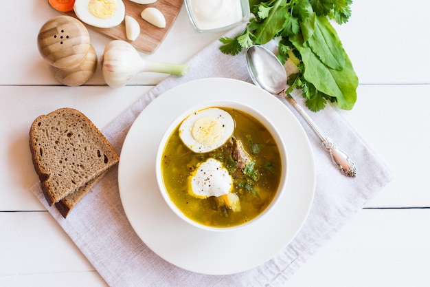 Sobre una mesa de tazón de madera blanca con sopa de verduras de primavera de acedera con crema agria y huevo de gallina. vista superior.