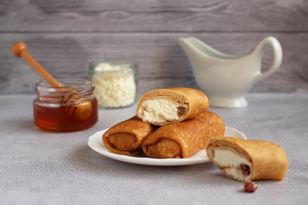 Sobre de panqueques finos rellenos de requesón y pasas en un platillo con miel en un respaldo gris