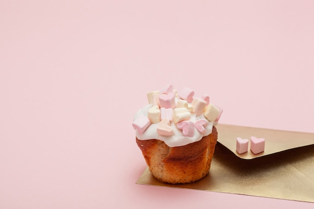 Sobre de papel dorado con dos corazones de malvavisco y cupcake de San Valentín aislado en rosa