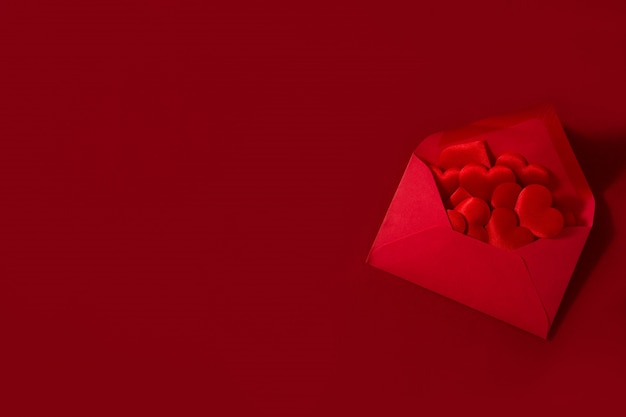 Sobre de papel rojo con corazones dentro aislado en superficie roja Concepto de San Valentín.