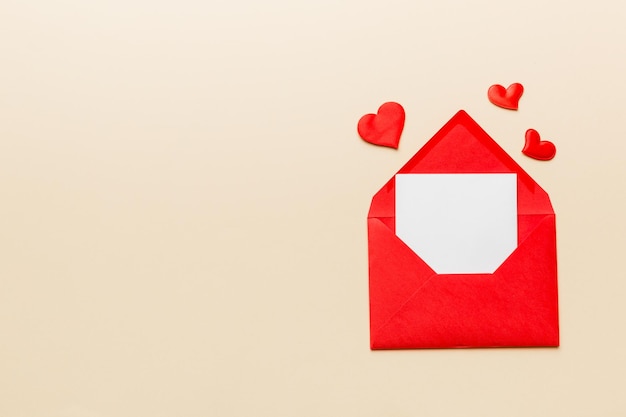 Sobre de papel rojo con tarjeta blanca vacía y corazón sobre fondo de color vista superior concepto de día de san valentín