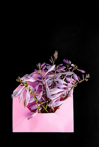 Sobre de papel rosa con flores frescas del jardín sobre fondo azul claro. Plantilla floral festiva. Diseño de tarjetas de felicitación. Vista superior. Tiro vertical.