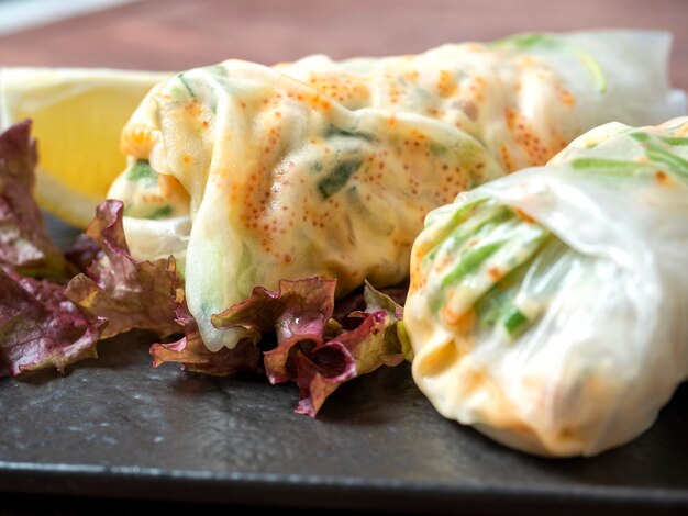 Sobre un plato de textura negra se enrollan rollitos de primavera. Un delicioso plato dietético. Cocina asiática, de cerca