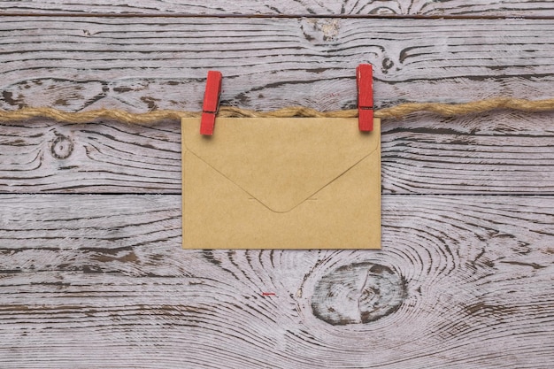 Un sobre postal cerrado en dos pinzas para la ropa de color rojo en una cuerda sobre un fondo de madera.