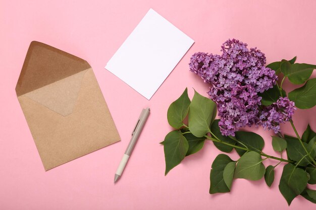 Sobre con ramas de lilas florecientes sobre fondo rosa Concepto de primavera Vista superior Endecha plana