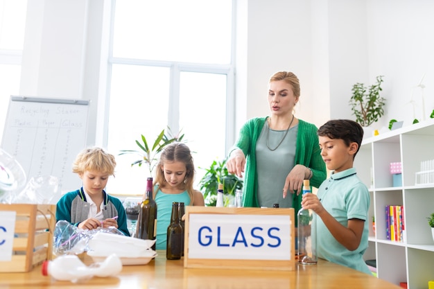 Sobre el reciclaje de vidrio. Maestra de escuela primaria contando a sus alumnos sobre el reciclaje de vidrio y la clasificación de residuos