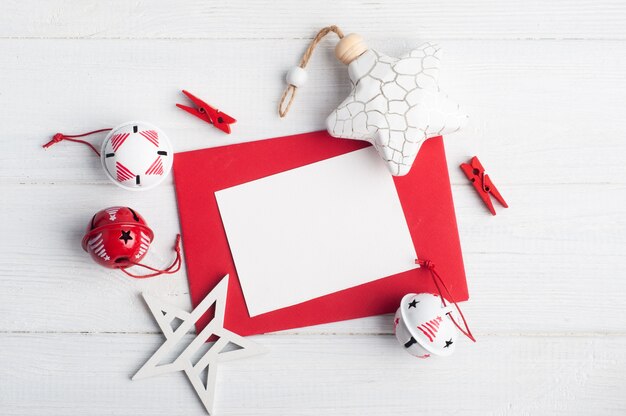 Sobre rojo en blanco, nota vacía y juguetes de Navidad blancos en madera rústica, endecha plana