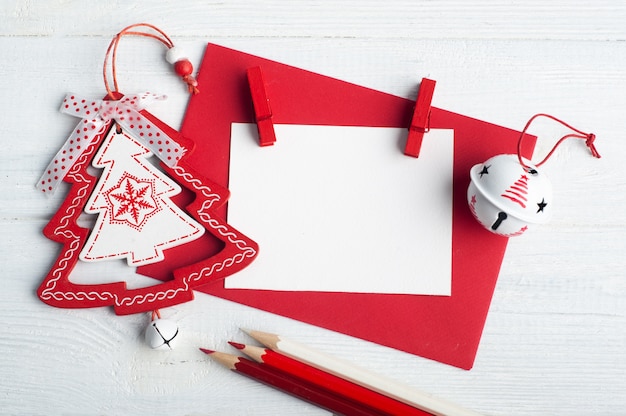 Sobre rojo en blanco, nota vacía y juguetes de Navidad blancos sobre fondo rústico de madera