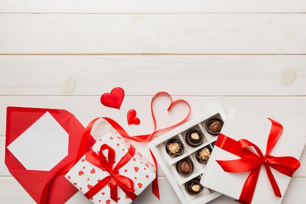 Sobre sobre fondo de color para el Día de San Valentín con caja de regalo y chocolate. En forma de corazón con caja de regalo de chocolates vista superior con espacio de copia.