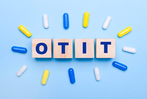 Sobre um fundo azul claro, comprimidos multicoloridos e cubos de madeira com o texto OTIT. Conceito médico