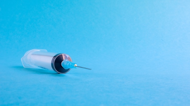 Sobre um fundo azul, encontra-se uma seringa médica com uma agulha. epidemia. Copie o espaço O conceito de coleta de sangue e vacinas injetáveis, equipamentos médicos para injeção hipodérmica, tema saúde.