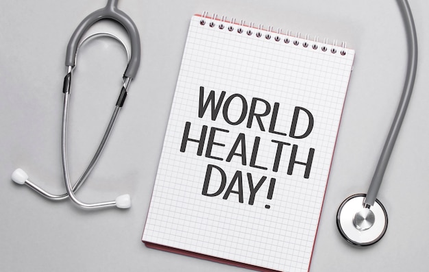 Sobre um fundo bege, um estetoscópio e um bloco de notas branco com a inscrição dia mundial da saúde.