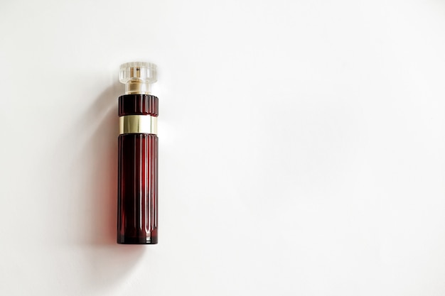 Sobre um fundo branco está um frasco de vidro para perfume de cor vermelho escuro.