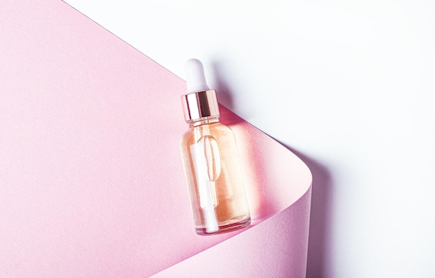 Sobre um fundo branco, um rolo de papel rosa claro enrolado e uma garrafa de vidro com óleo amarelo. O conceito de beleza e medicina