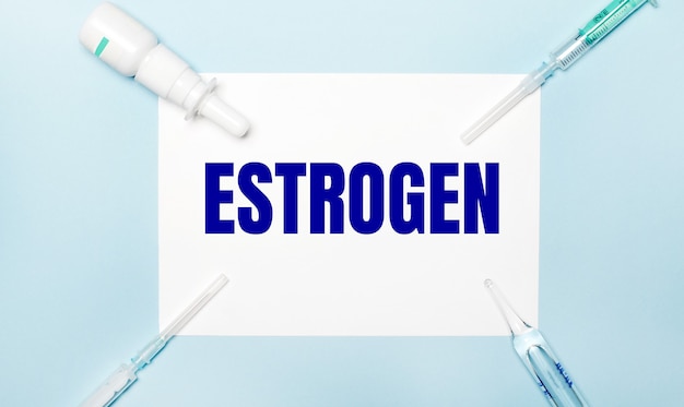 Sobre uma superfície azul clara, seringas, um frasco de remédio, uma ampola e uma folha de papel branca com o texto estrogen