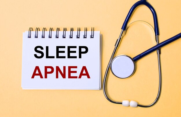 Sobre uma superfície bege, um estetoscópio e um bloco de notas branco com a inscrição SLEEP APNEA. Conceito médico