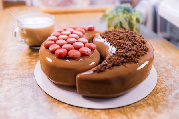 Sobre una vieja mesa de madera hay una hermosa tarta de chocolate, una taza transparente con café y una pequeña planta.