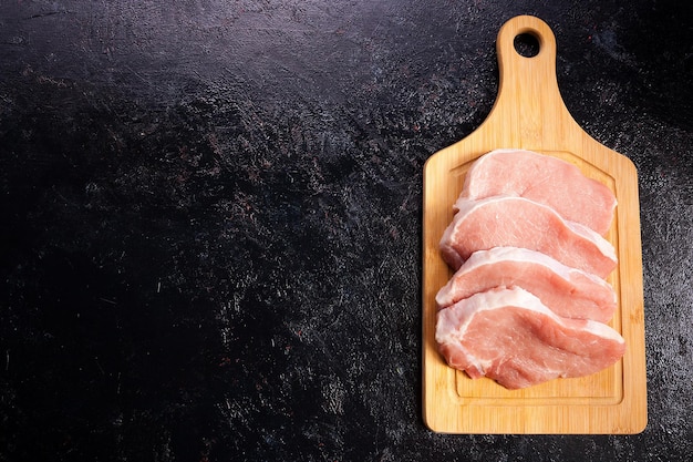 Sobre la vista superior de cuatro piezas de carne de bistec cruda fresca sobre una tabla de madera sobre fondo de madera negra. Comida gourmet y comida fresca sin cocinar