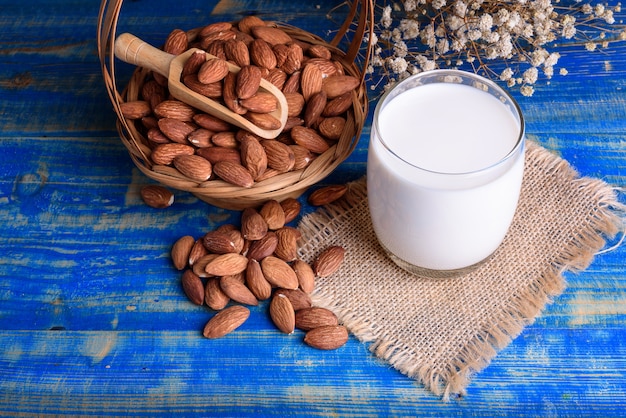 Sobre la vista vaso de leche con cuchara de madera y almendras en la mesa de madera azul.