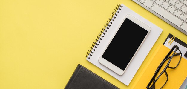 Sobrecarga de fotos de gafas de portátil clips portapapeles teléfono teclado y carpeta aislado en el fondo amarillo