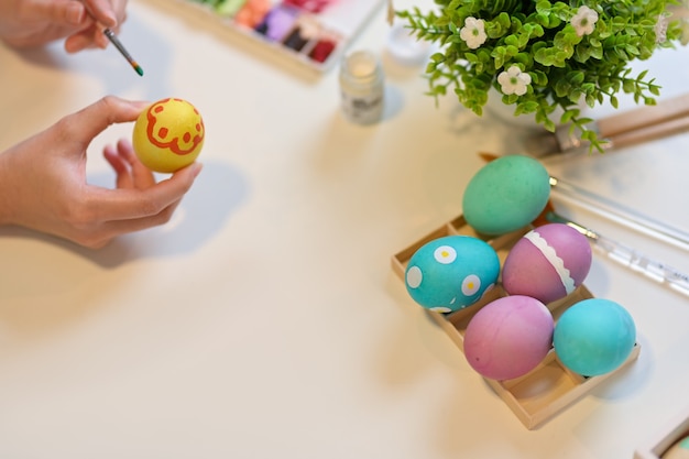 Sobrecarga de manos femeninas pintando huevos para prepararse para el festival de Pascua en mesa de artesanía con herramientas de pintura