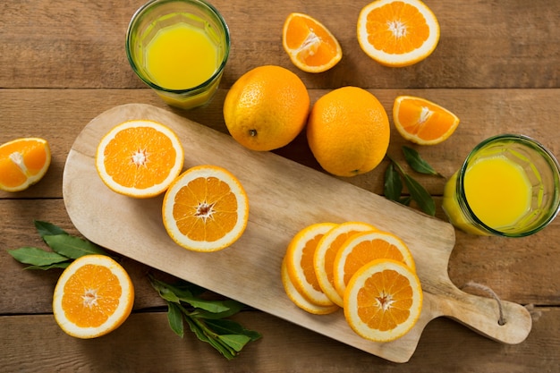 Sobrecarga de naranjas con vasos de jugo en la mesa de madera