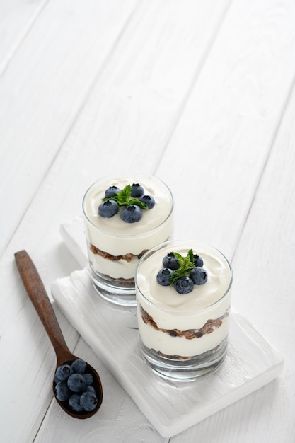 Sobremesa com mirtilos frescos de queijo cottage e granola em um copo sobre um fundo branco de madeira