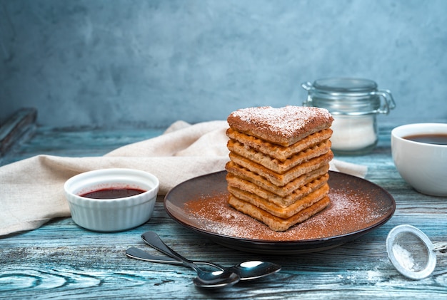 Sobremesa com waffles com açúcar de confeiteiro em um prato marrom sobre fundo cinza-azulado.