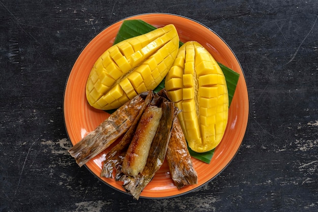 Sobremesa de estilo tailandês manga amarela com arroz pegajoso de banana em folhas de palmeira Manga amarela e arroz pegajoso é comida tradicional popular da Tailândia Closeup