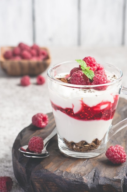 Sobremesa de framboesa ou café da manhã com iogurte natural em uma caneca de vidro e framboesas maduras
