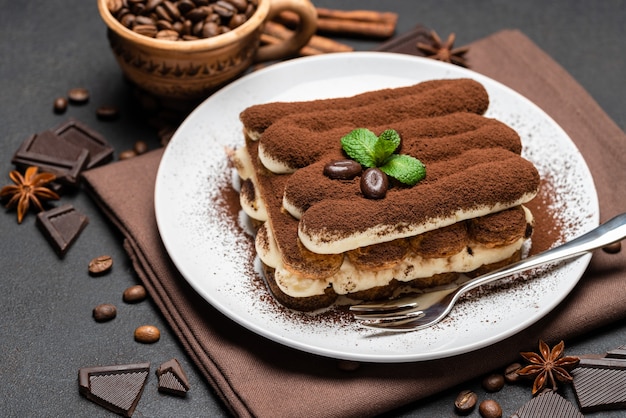 Sobremesa de tiramisu clássico em um prato de cerâmica em fundo escuro de concreto