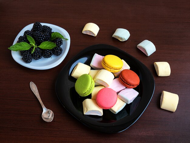 Sobremesa de verão e biscoitos coloridos: amora e hortelã folhas em um prato. Marshmallow, macarons em uma mesa de madeira