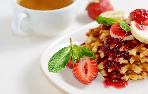 Sobremesa de waffles com morango, banana e hortelã. xícara de chá para café da manhã saudável