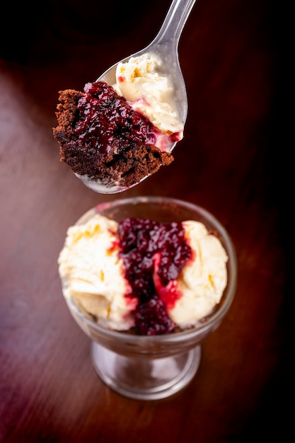 Sobremesa de xícara de sorvete com degustação de molho de brownie e berry com colher closeup