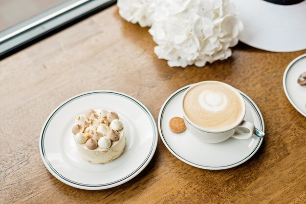 Sobremesa deliciosa e uma xícara de café na mesa. desfrute de uma sobremesa recém-assada em um café, restaurante. uma dose de close up de um pequeno bolo decorativo doce e um cappuccino. foco seletivo suave.