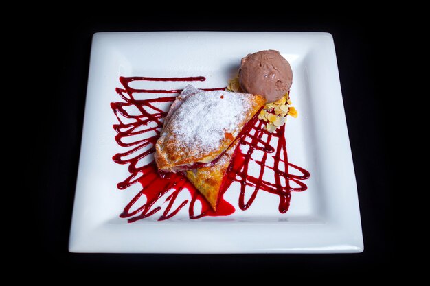 Sobremesa doce saborosa. Torta de morango arejada com açúcar de confeiteiro, geléia de morango, pedaços finos de avelã e uma porção de sorvete de chocolate. Fundo preto