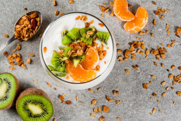 Sobremesa saudável de granola de iogurte de tangerina e kiwi no café da manhã, com ingredientes, mesa de pedra cinza, cópia espaço vista superior