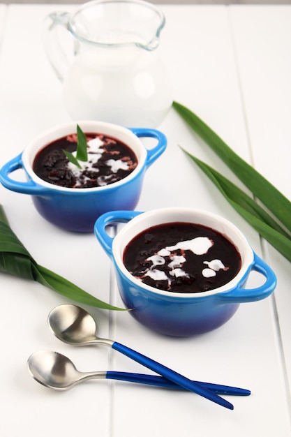 Sobremesa Tradicional Indonésia: Bubur Ketan Hitam ou Mingau de Arroz Glutinoso Preto, Servido com Molho de Leite de Coco e Guarnecido com Folhas de Pandan. Two Bowl, Fundo Branco, Close Up