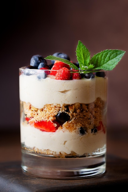 Sobremesa vegana doce em um copo com chantilly de menta de bagas e biscoito em um fundo marrom