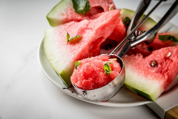 Sobremesas de frutas de verão, coquetéis congelados. Granito de sorvete de melancia com hortelã, uma colher na colher de sorvete, no prato com fatias de melancia.