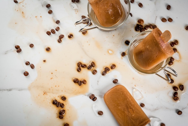 Sobremesas de verão. Bebidas congeladas. Picolés doces feitos de café e leite. Em xícaras de café, em uma mesa de mármore branco, com grãos de café. vista do topo