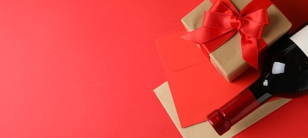 Sobres, caja de regalo y botella de vino sobre fondo rojo.