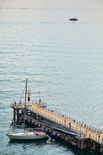 Sochi, Rússia. Iate de vela no cais contra o mar calmo e um pequeno barco ao longe.