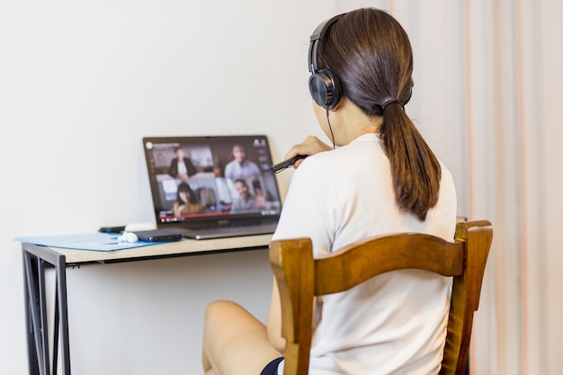 Foto social distanciando mulher usando fone de ouvido durante a vídeo chamada em grupo com os amigos.