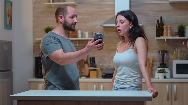 Socio enojado pidiendo explicaciones por mensajes. Hombre celoso engañado enojado frustrado ofendido irritado acusando a la mujer de infidelidad discutiéndola con fotos del teléfono inteligente gritando desesperada