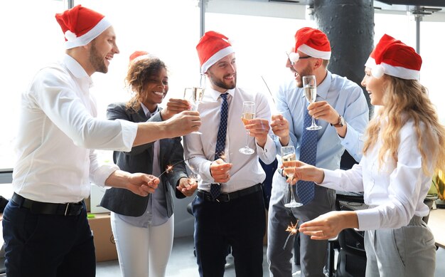 Socios comerciales jóvenes encienden luces de bengala y beben champán en una oficina moderna. Feliz navidad y próspero año nuevo.