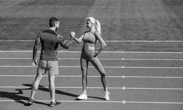 Los socios deportivos, hombres y mujeres, celebran la victoria del equipo con un gesto de estrechar la mano después de hacer ejercicio o competir en la lucha de brazos en el éxito del deporte al aire libre en la pista de atletismo del estadio