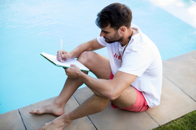 Socorrista escribiendo en el portapapeles junto a la piscina en un día soleado