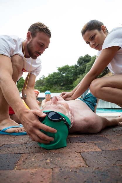 Socorristas masculinos y femeninos presionando el pecho del hombre mayor inconsciente junto a la piscina