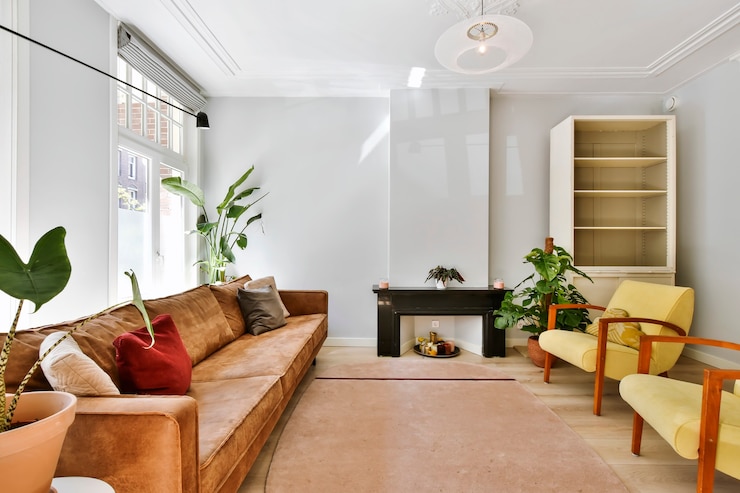 Foto sofá confortável de couro e poltronas coloridas com planta monstera em uma sala bem iluminada com teto ornamental